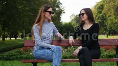 在阳光明媚的一天，两个女朋友在公园里坐在长凳上聊天